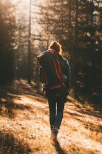 A woman backpacker walks through a sunlit forest trail, embracing nature and adventure.